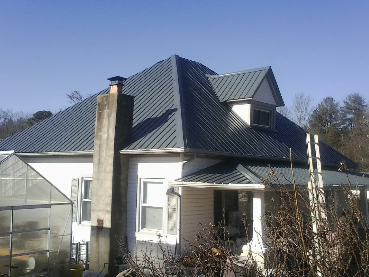 Dark blue standing seam metal roof on a white farmhouse with dormer — Slate & Tile Roof Repair by Roofing Brothers in Perrinton