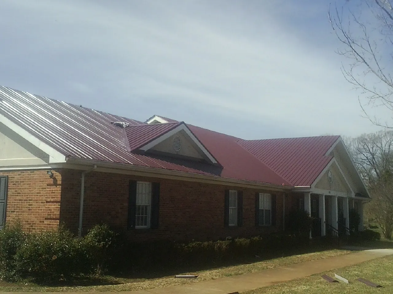 Red metal roof with gabled entries on a long brick building, from a Hail Damage Roof Repair job in Perrinton