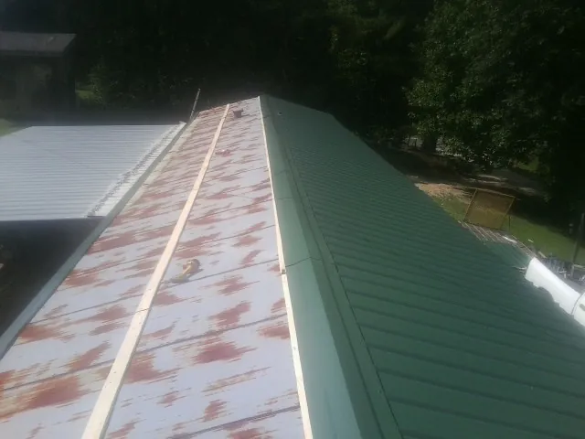 Old rusted panels beside newly installed green metal roofing — Wind Damage Roof Repair by Roofing Brothers in Perrinton
