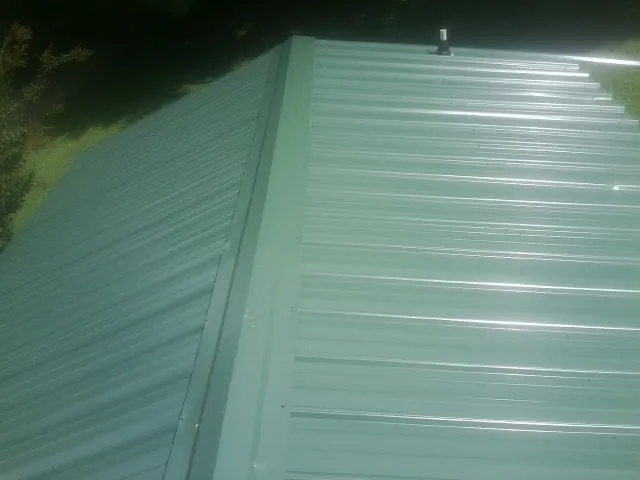 New green metal panels meeting at the ridge of a roof — Flat Roof Repair work by our crew in Perrinton
