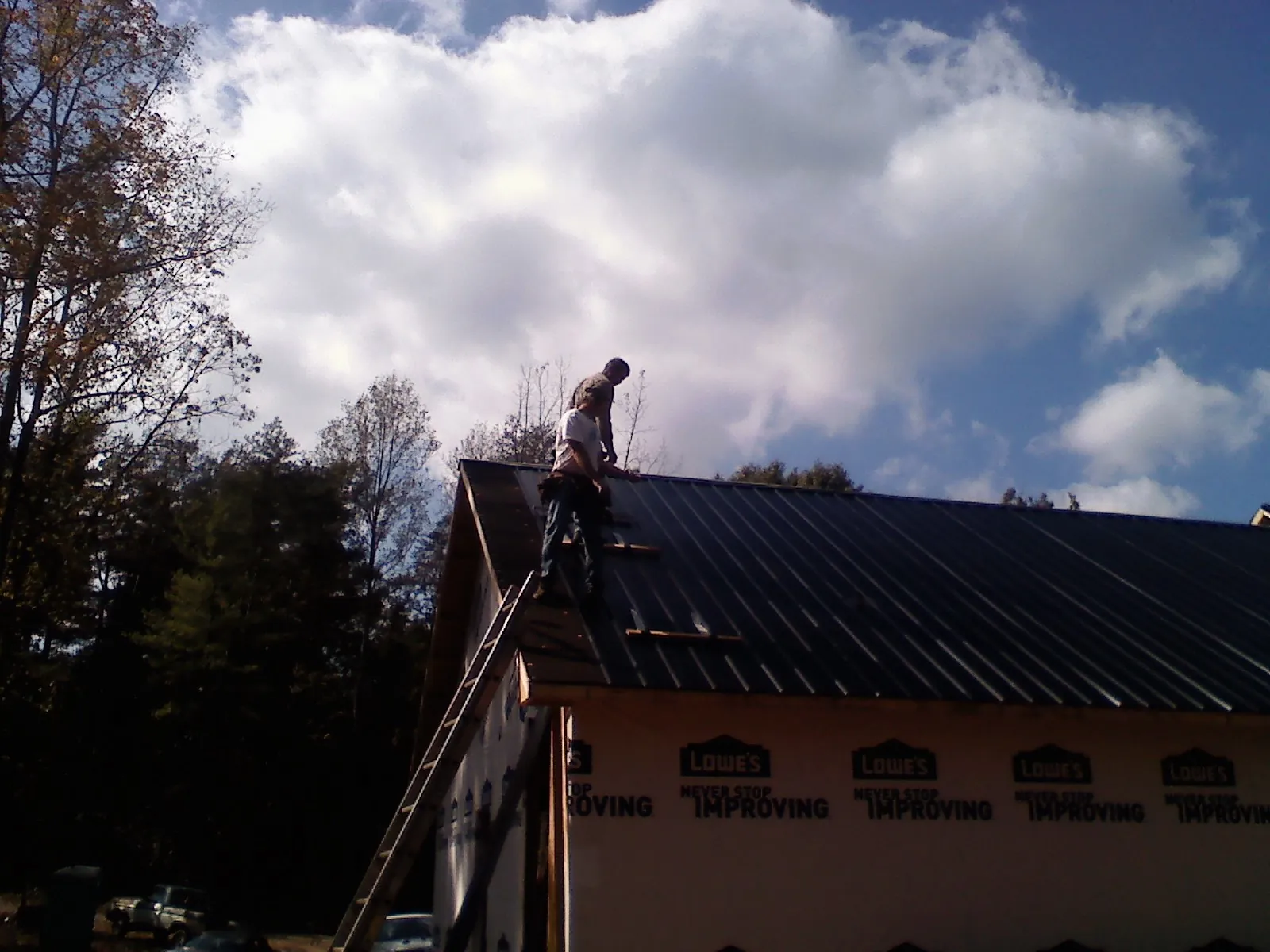 Roofer fastening dark metal panels high against a cloudy sky, from a Roof Inspection job in Perrinton