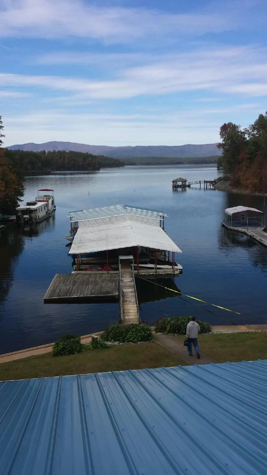 View across a lake from a newly installed blue metal roof in Perrinton