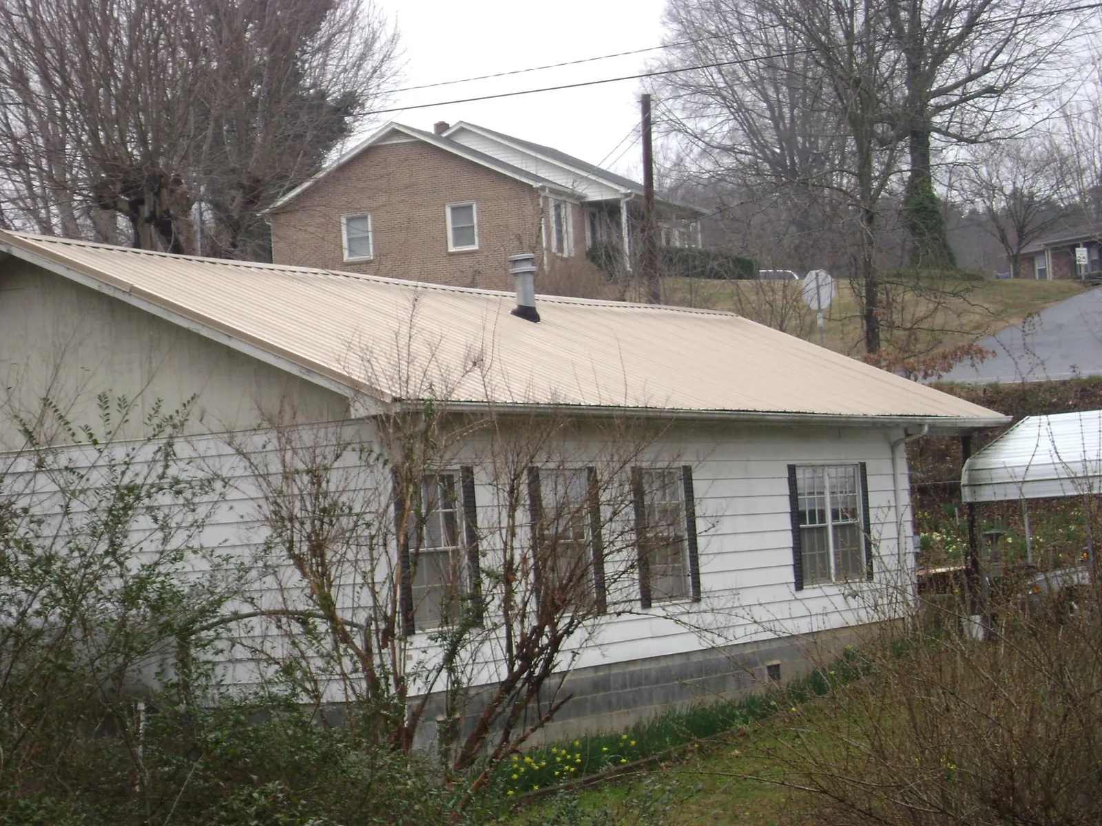 Tan metal roof on a white sided house set into a hillside — Commercial Roofing by Roofing Brothers in Perrinton