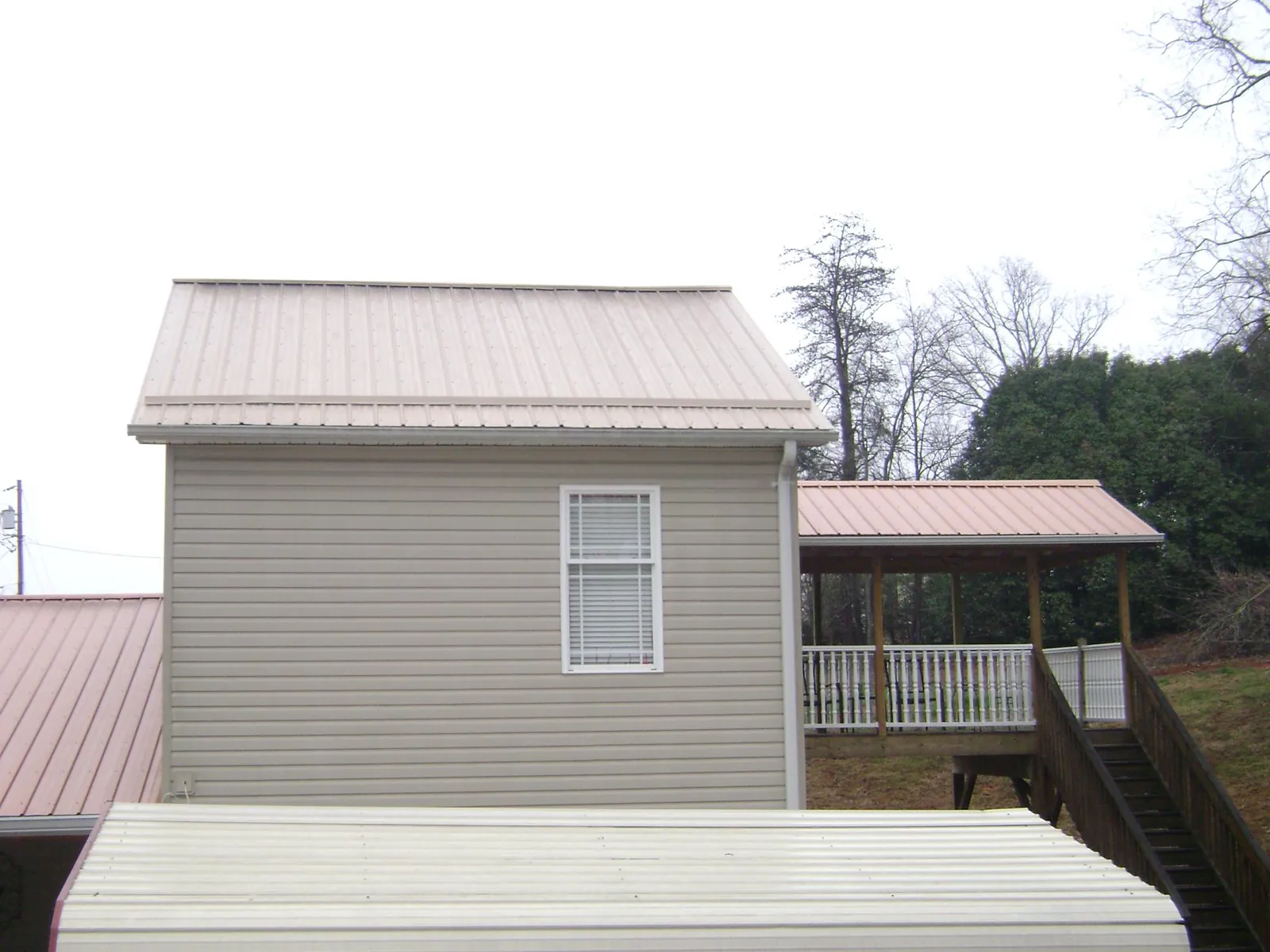 Tan metal roofs on a two story addition and attached porch, from a Roof Replacement job in Perrinton